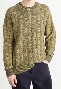 Sweter dziany z wzorem jodełki w kolorze zielonym i żółtym, z okrągłym dekoltem, luźnym krojem oraz ściągaczami na rękawach i dole.