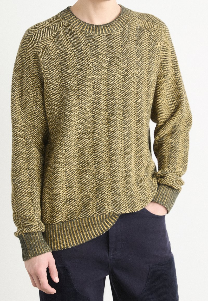 Sweter dziany z wzorem jodełki w kolorze zielonym i żółtym, z okrągłym dekoltem, luźnym krojem oraz ściągaczami na rękawach i dole.
