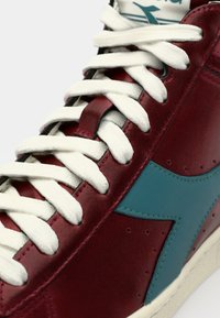 Red and teal high-top sneaker featuring white laces, leather material, perforated detailing, and a prominent teal brand logo on the side.