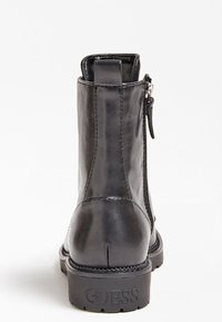 Bottine en cuir noir avec une finition lisse, fermeture éclair et semelle en caoutchouc texturé. Détail du logo embossé sur le talon.