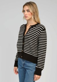 Cardigan rayé noir et blanc avec un devant à boutons, des poignets et un ourlet côtelés, fabriqué en mélange de laine douce, associé à un jean bleu.