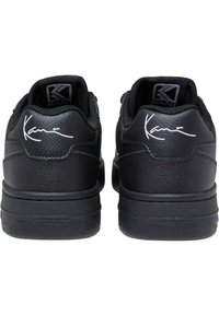 Schwarze Sneakers mit einem glatten Leder-Obermaterial, gepolsterten Kragen, charakteristischen weißen Details und strukturierten Gummisohlen.