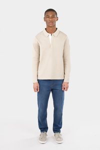 Beige Langarmpoloshirt mit weißem Kragen, kombiniert mit blauer Jeans und hellgrauen Sneakers. Einfaches Design, Baumwollstoff.