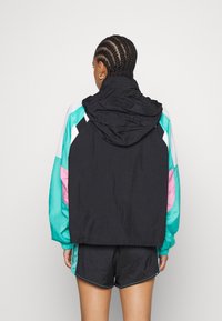 Větruodolná bunda v černé barvě s akcenty v tyrkysové, rů žové a bílé. Má kapuci, elastické manžety a texturovaný, lehký materiál.