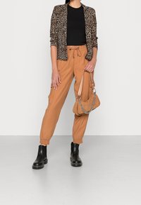 Marynarka w wzór panterki, czarny t-shirt, pomarańczowe spodnie cargo i czarne buty chelsea. Całość dopełnia torebka na ramię w teksturowanym odcieniu brązu z łańcuszkiem.
