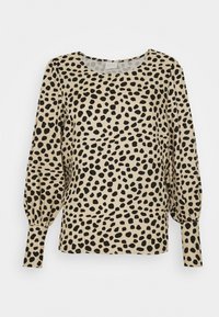 Blouse beige avec des taches noires irrégulières, manches longues bouffantes, encolure ronde et poignets froncés. Tissu doux et léger.