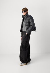 Casaco puffer preto com um design cropped, combinado com calças largas pretas. Camisola cinza por baixo, e sapatilhas prateadas completam o look.