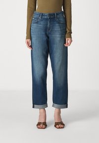 Donkerblauwe denim jeans met een hoge taille, rechte pijpen, opgerolde manchetten en een klassieke vijf-pocket design. Gemaakt met bruine sandaalbanden.