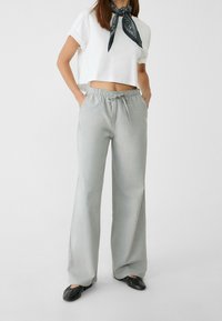 Jasnoszare szerokie spodnie z elastycznym pasem i regulowanym sznurkiem. Połączone z krótkim białym topem i czarną wzorzystą chustą.