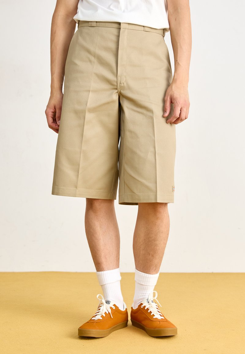 Beige knee-length shorts with a flat front, tailored fit, and belt loops, paired with orange sneakers and white socks.