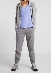 Grå zip-up fleecejacka, ljuslila linne, grå byxor och grå/svarta skor. Avslappnad atletisk look med en avslappnad passform.