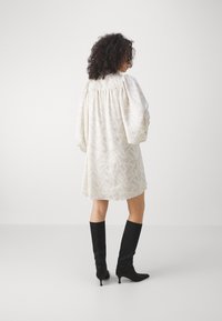 Abito a maniche lunghe di colore crema con motivo testurizzato, retro arricciato e vestibilità ampia, abbinato a stivali neri in suede al ginocchio con tacchi inclinati.