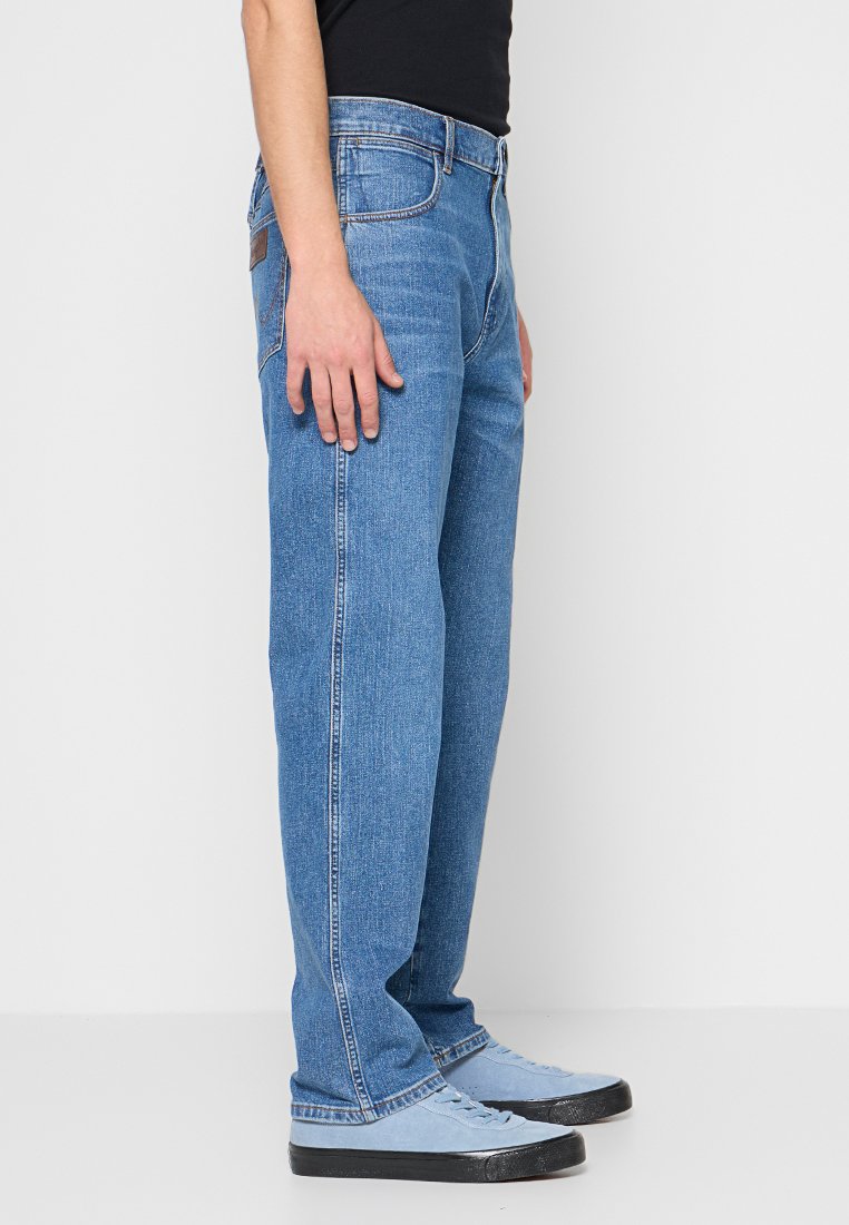 Niebieskie dżinsy z prostymi nogawkami, w klasycznym pięcio-kieszeniowym stylu, z brązową skórzaną naszywką na tylnej części pasa.