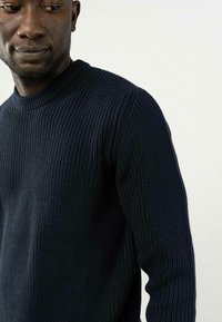 Marineblau gestrickter Pullover mit einem strukturierten Rippenmuster. Verfügt über einen Rundhalsausschnitt und lange Ärmel, hergestellt aus einem weichen, dehnbaren Stoff.