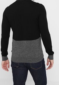 Schwarzer und dunkelgrauer Strickpullover mit einem Farbblock-Design. Er verfügt über einen runden Ausschnitt und lange Ärmel mit gerippten Bündchen.