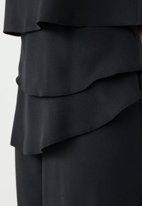 Schwarzer, geschichteter Stoff mit weichem Fall. Drei horizontale Rüschen schaffen Textur und visuelles Interesse, mit glatten Kanten und ohne Muster.