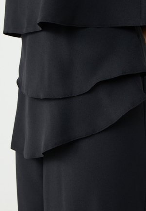 Tessuto nero a strati con una caduta morbida. Tre ruffle orizzontali creano texture e interesse visivo, con bordi lisci e senza motivi.