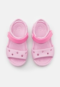 Vaaleanpunaiset muotilla valmistetut sandaalit, joissa on kaksi leveää hihnaa, pyöreitä tuuletusaukkoja ja texturoitu pohja. Säädettävä kantahihna varmistaa turvallisen istuvuuden.