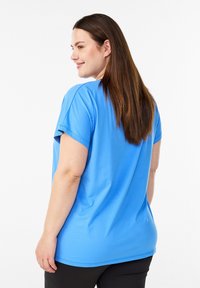 Locker geschnittenes Kurzarmhemd in leuchtendem Blau aus glattem Stoff. Rundhalsausschnitt und saubere Nahtdetails. Kombiniert mit dunkler Hose.