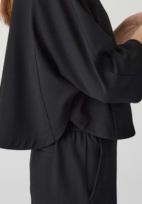 Black pullover with wide sleeves, featuring a loose fit and visible stitching details. The fabric appears smooth and slightly textured.