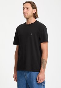 Camiseta de algodón negra con cuello redondo y mangas cortas, que presenta un pequeño logo blanco en el pecho y un corte relajado.