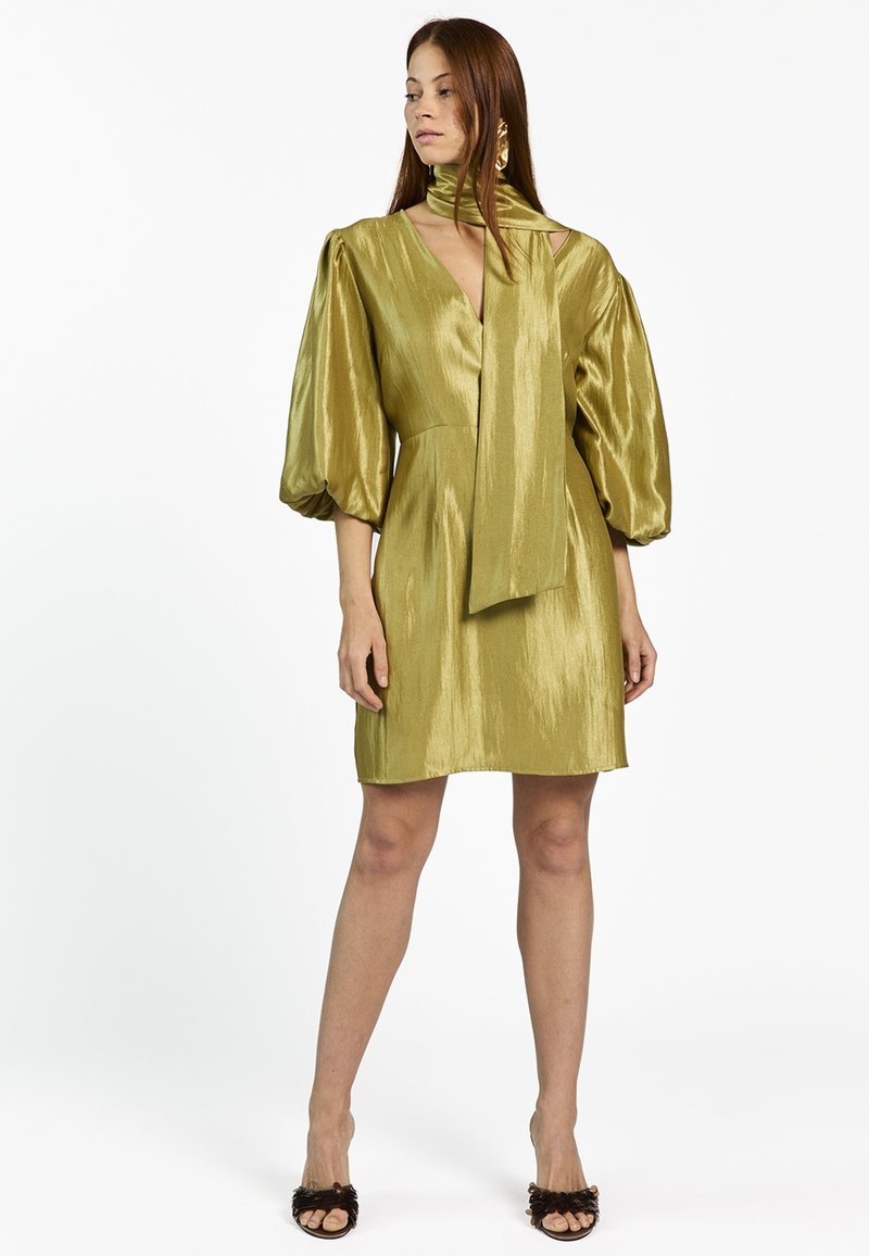 Limoengroene satijnen jurk met een diepe V-hals, ballonmouwen en een nekstrik. Gladde textuur met een zoom tot op de knie en een semi-aansluitend ontwerp.