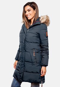 Námornícka puffer bunda s kapucňou lemovanou kožušinou, zipsovými vreckami, prešívanou textúrou a jemným brandingom na rukáve. Dĺžka presahuje boky.