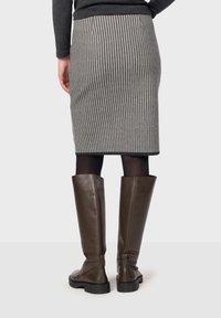 Rutig blyertskjol i svart och vitt med en figurnära design, kombinerad med knähöga bruna läderstövlar och svarta ogenomskinliga tights.