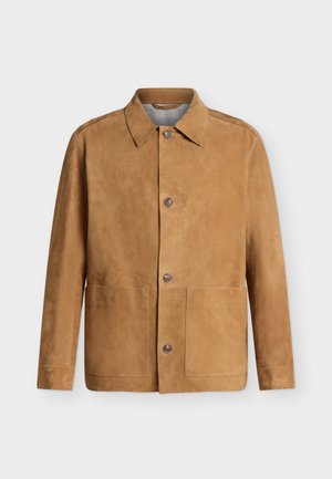 Veste en daim beige à boutons, col pointu et deux grandes poches avant, affichée sur un fond clair uni.