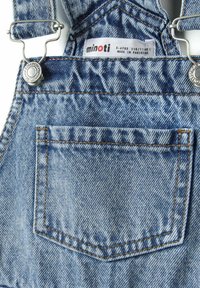 Salopette en denim bleu clair avec des décolorations visibles, des bretelles métalliques réglables et une petite poche arrière. L'étiquette indique une taille de 5-6 ans.