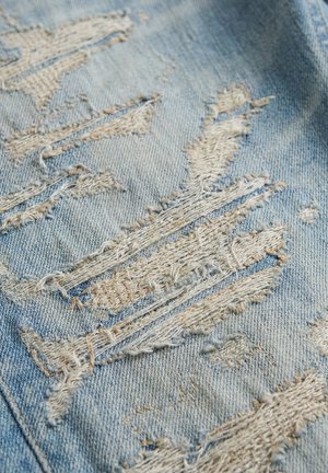 Lichtblauwe denimstof met meerdere rafelige en gescheurde distressed stukken die witte draden tonen.