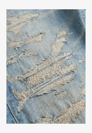 Lichtblauwe denimstof met meerdere rafelige en gescheurde distressed stukken die witte draden tonen.