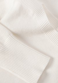 Biały sweter dzianinowy z prążkowanym mankietem i gładką fakturą. Materiał wydaje się miękki, z lekkim, jednolitym splotem w całej powierzchni.