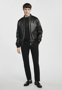 Czarna skórzana kurtka bombowa z zapięciem na zamek, ściągaczami na rękawach i gładkim wykończeniem, w połączeniu z czarną koszulą i dopasowanymi czarnymi spodniami.
