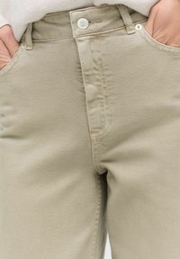 Beige bomullschinos med knappstängning, två framfickor och en slät yta. Tyget har subtila sömnadsdetaljer.