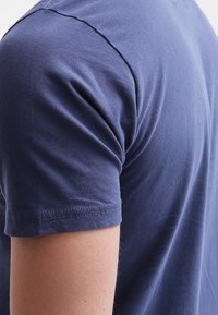 Námorně modré bavlněné tričko s kulatým výstřihem a krátkými rukávy; hladká textura s viditelným prošíváním na švech.