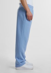Lyseblå sweatpants lavet af blød bomuldsblanding, med elastisk talje, sidelommer og tapered ben. Hvide sneakers komplementerer outfittet.