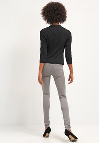 Musta räätälöity bleiseri, jossa on kolme neljäsosan hihaa, yhdistetty vaaleanharmaisiin kapeisiin farkkuihin ja mustiin korkokenkiin, nähtynä takaa.