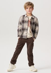 Grijze geruite flanellen overhemd, beige graphic t-shirt, bruine sportbroek, witte sneakers. Relaxed fit, knoopsluiting aan de voorkant en zijzakken.