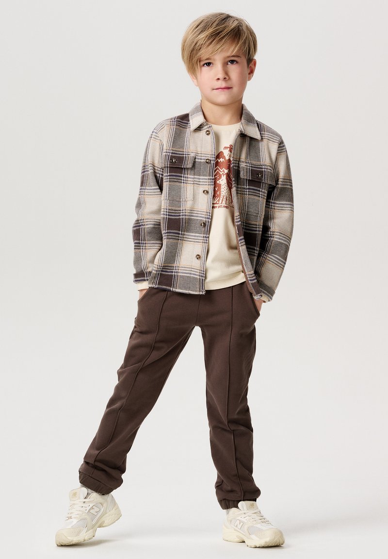 Grijze geruite flanellen overhemd, beige graphic t-shirt, bruine sportbroek, witte sneakers. Relaxed fit, knoopsluiting aan de voorkant en zijzakken.