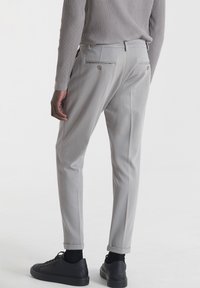 Pantaloni grigi chiari con una vestibilità su misura, dotati di due tasche posteriori, cuciture sottili e risvolti. Abbinati a sneakers nere.