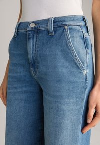 Light blue denim jeans featuring a high waist, straight leg design, subtle whiskering, and silver-tone hardware on pockets.
