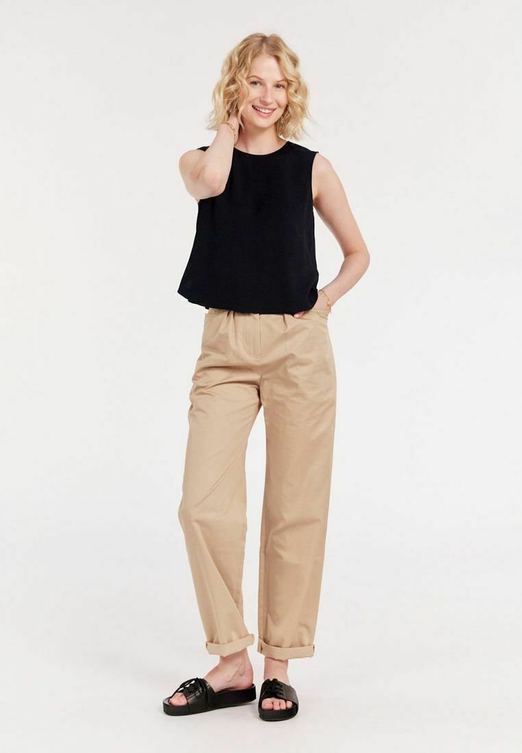 Haut sans manches noir, pantalon beige taille haute et sandales noires à enfiler. Tenue décontractée avec une coupe ample et des revers aux pantalons.