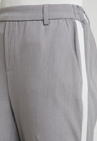 Grijs taps toelopende broek met een textuurstof, voorzien van een witte zijstreep en voorkruiden. Elastische tailleband voor comfort.