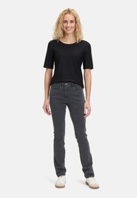 Haut noir texturé à manches courtes associé à un jean gris ajusté. La tenue comprend des chaussures blanches avec des accents beiges. Design simple et moderne.