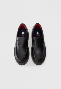 Schwarze Lederloafer mit runder Spitze, kontrastierenden hellen Nähten und einer strukturierten Seite. Das Innere verfügt über rote Akzente und Branding.