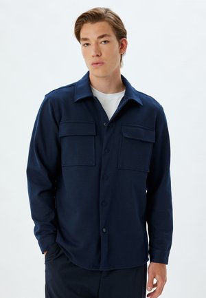 Donkerblauwe langjarige shirt met een knoopsluiting aan de voorkant, twee borstzakken en een klassieke kraag, gemaakt van gestructureerde stof.