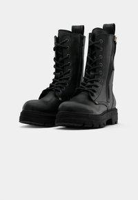 Zwarte leren veterschoenen voor in de strijd met zijritsen en dikke, grofgebekte zolen op een witte achtergrond.