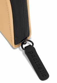 Funda con cremallera en color marrón con acentos de tela negra y una etiqueta de goma negra que presenta la palabra embozada "pactastic". Textura suave y forma rectangular.
