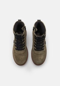 Oliwkowe zamszowe buty high-top z czarnymi sznurowadłami, o teksturowanej powierzchni i brązowej gumowej podeszwie. Posiadają zamki błyskawiczne po bokach.